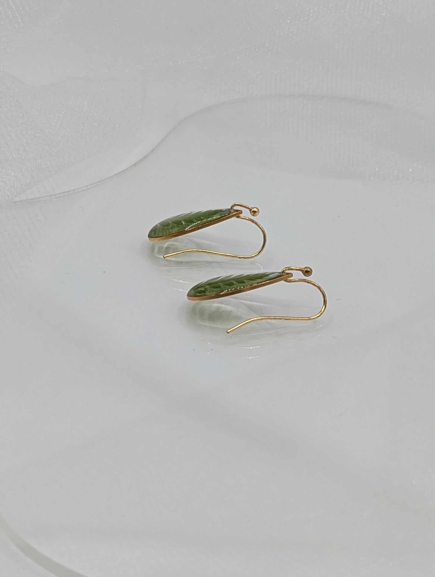 Gold earrings with green leaves on a white background