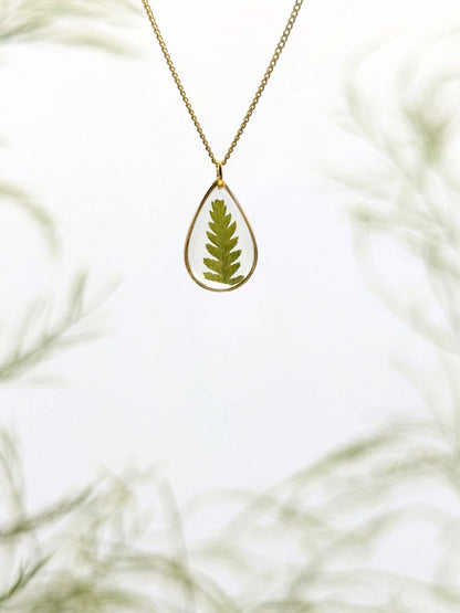 Gold necklace with a teardrop-shaped pendant featuring a pressed green leaf on a white background.