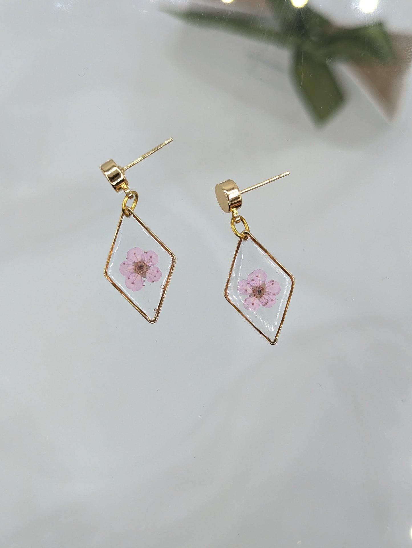 Gold geometric earrings with pink floral design on a light background
