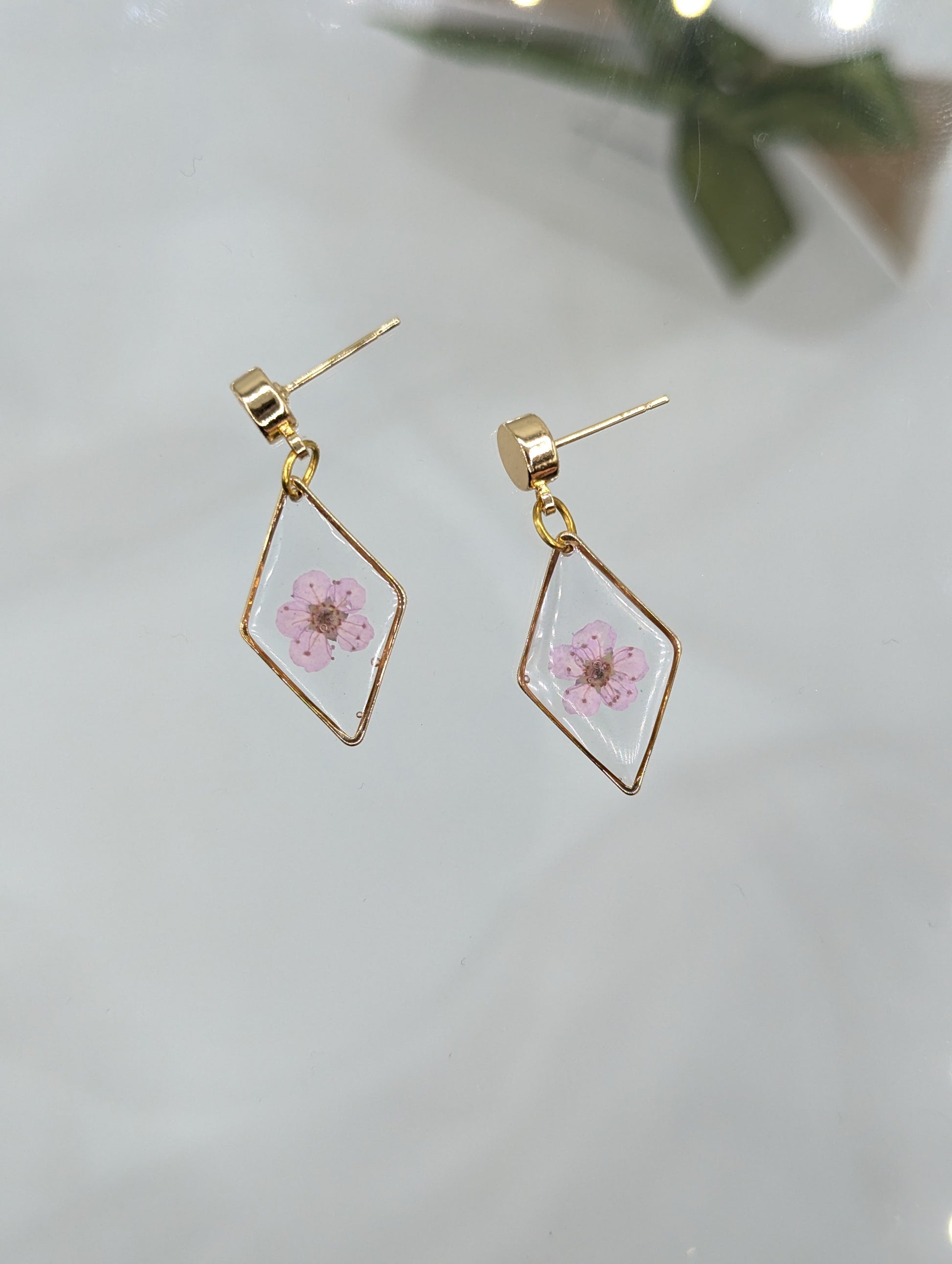 Gold geometric earrings with pink floral design on a light background