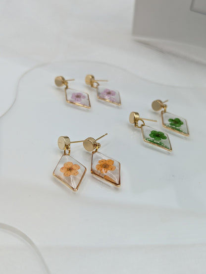 Set of four diamond-shaped earrings with floral designs on a white surface