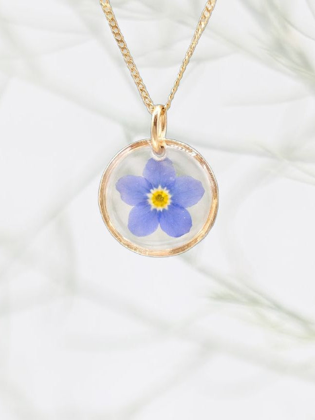 Gold necklace with a blue flower pendant on a white fabric background