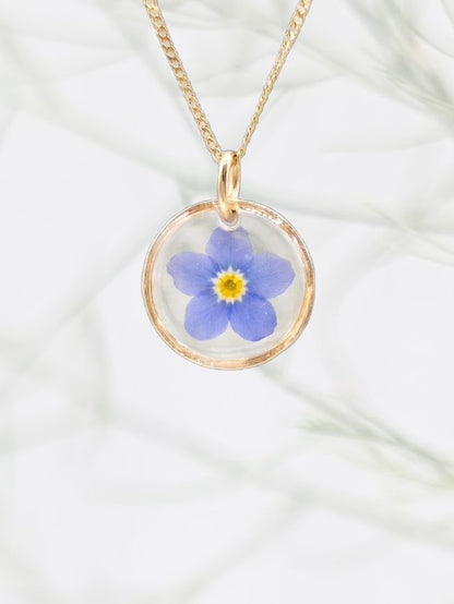 Gold necklace with a blue flower pendant on a white fabric background