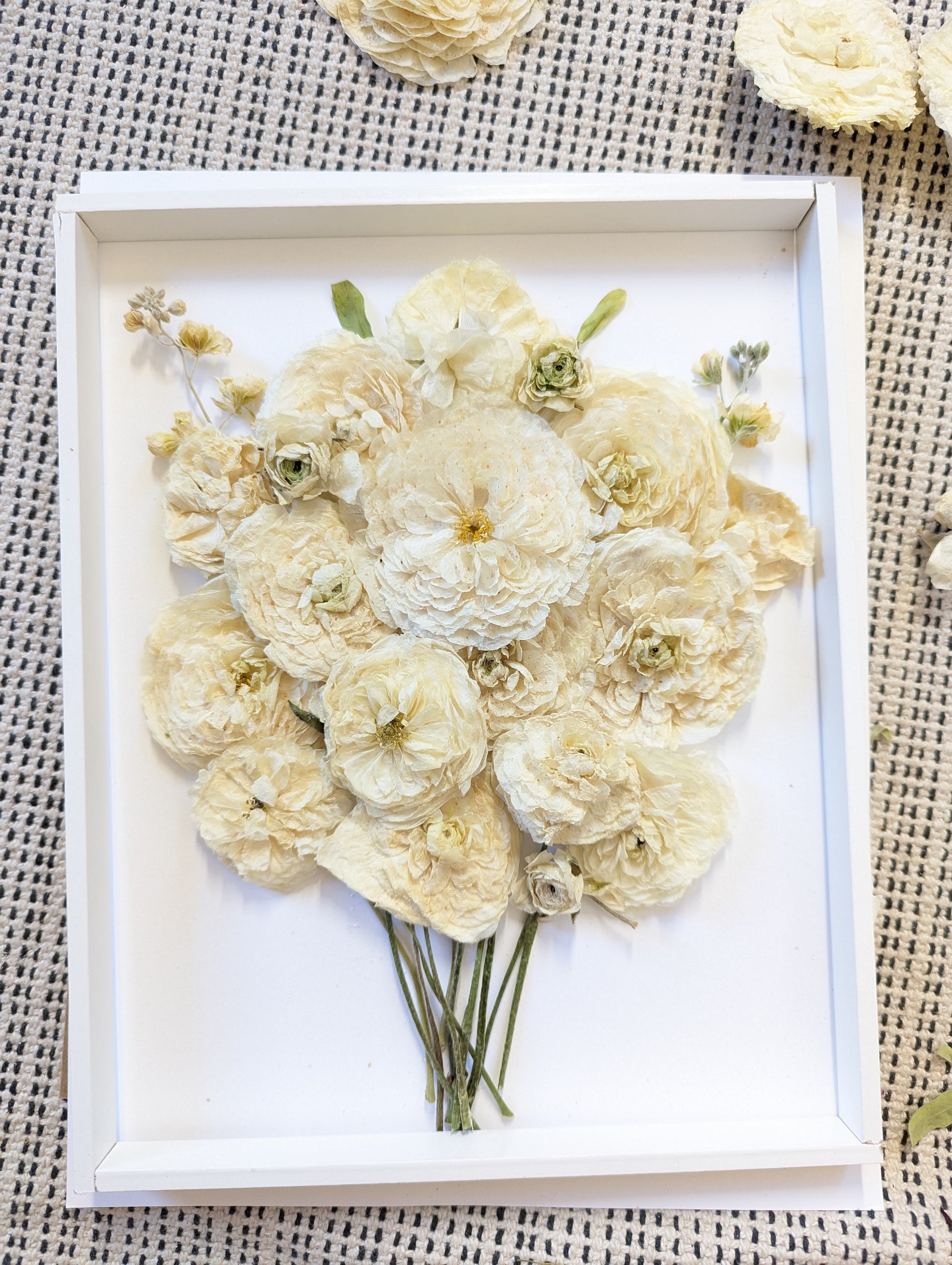 Pressed flower arrangement in a white frame on a textured surface