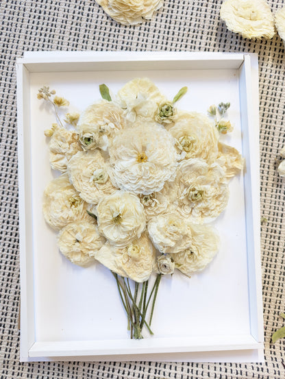 Pressed flower arrangement in a white frame on a textured surface