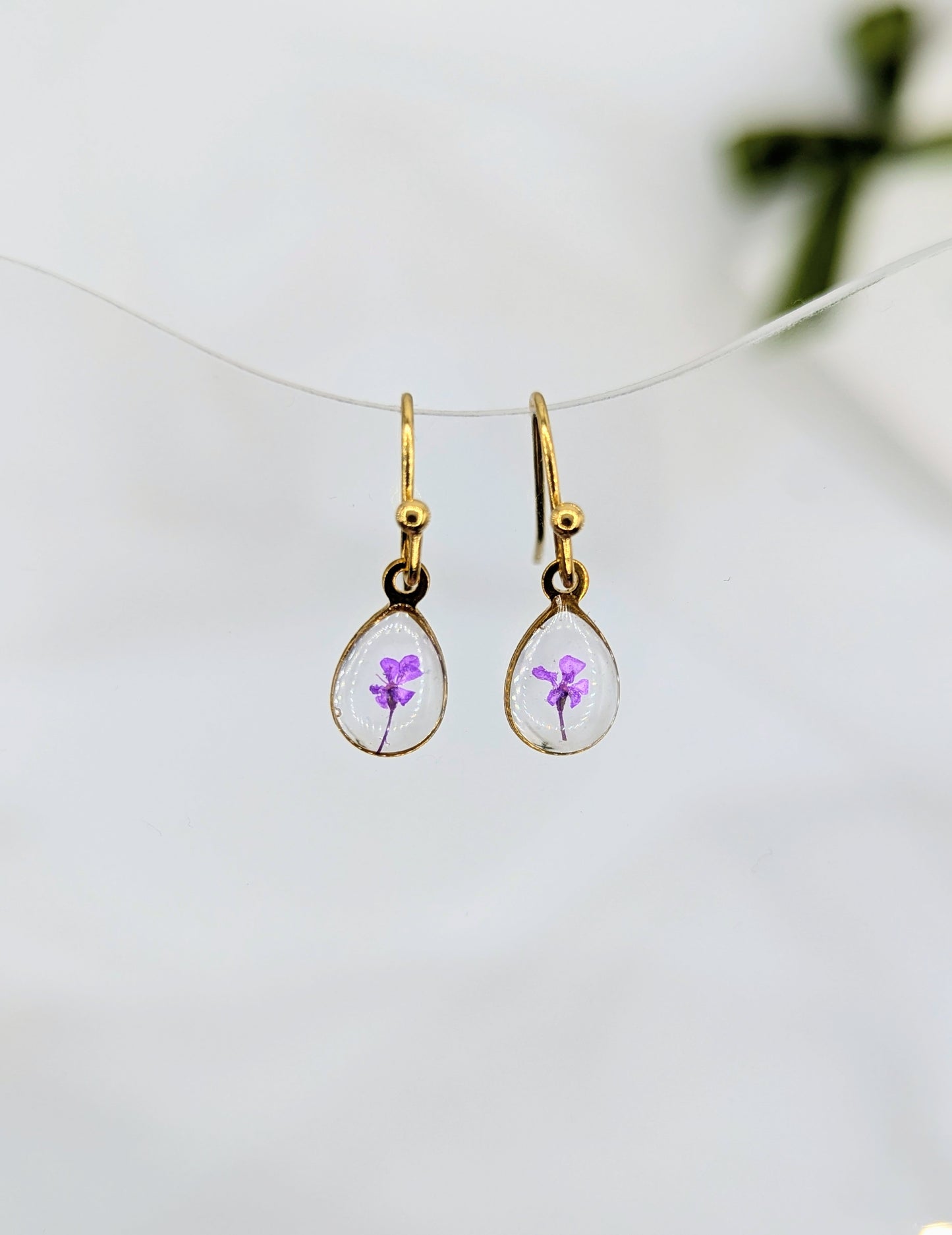 Teardrop-shaped earrings with purple flowers inside on a white background