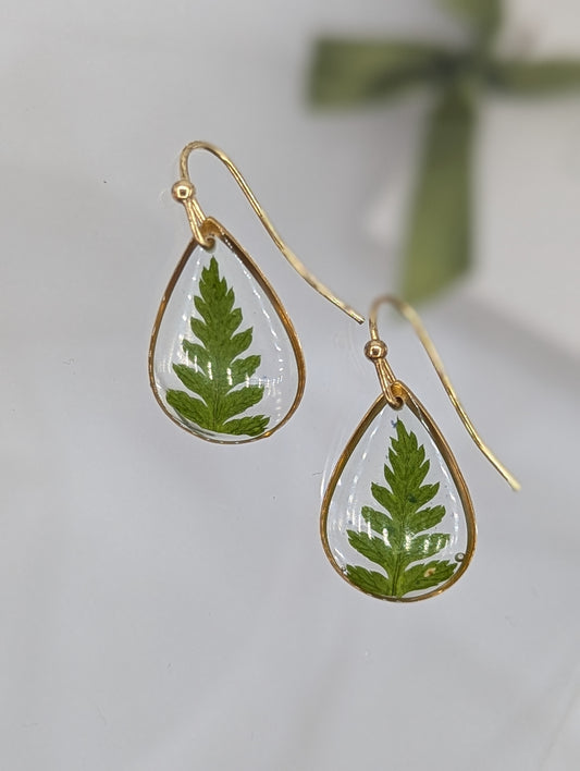 Teardrop-shaped earrings with green leaf designs on a light background