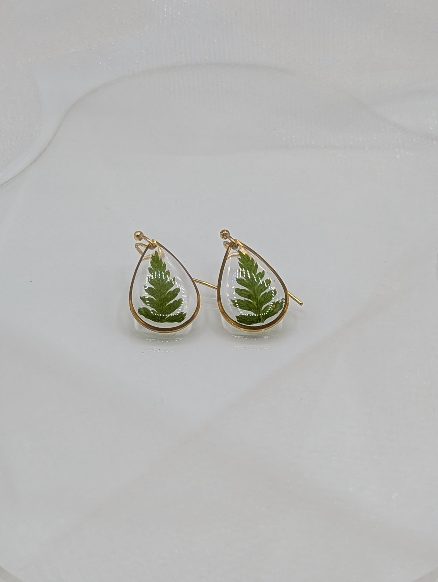 Teardrop-shaped earrings with green leaf designs on a light gray background