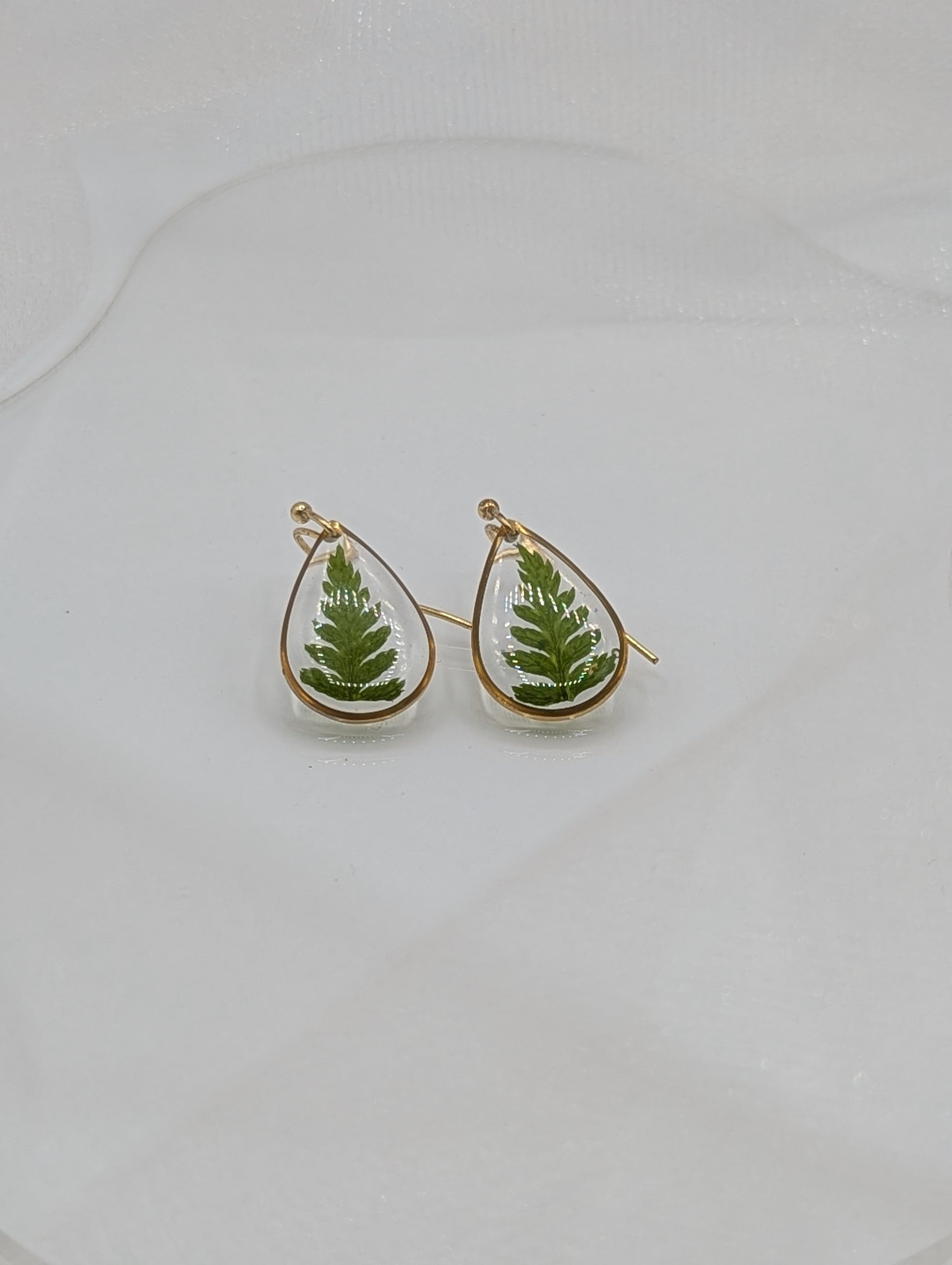 Teardrop-shaped earrings with green leaf designs on a light gray background