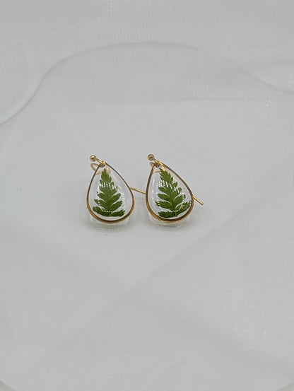 Teardrop-shaped earrings with green leaf designs on a light gray background