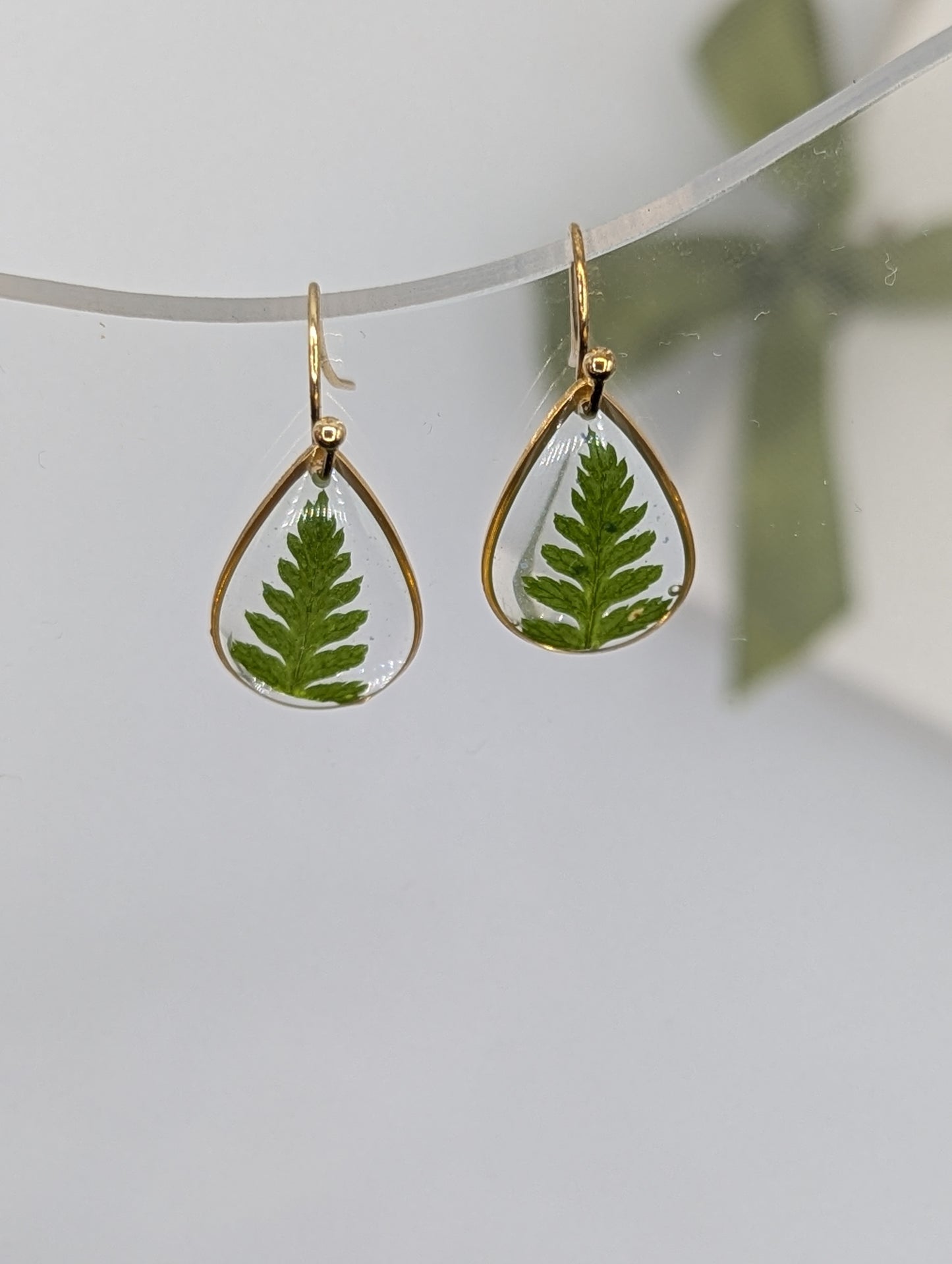 Teardrop-shaped earrings with green leafy interior on a light gray background