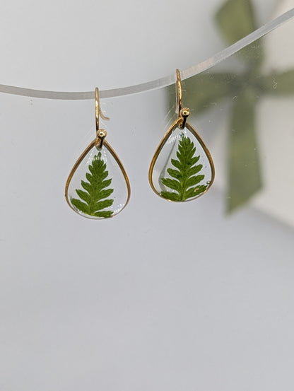 Teardrop-shaped earrings with green leafy interior on a light gray background