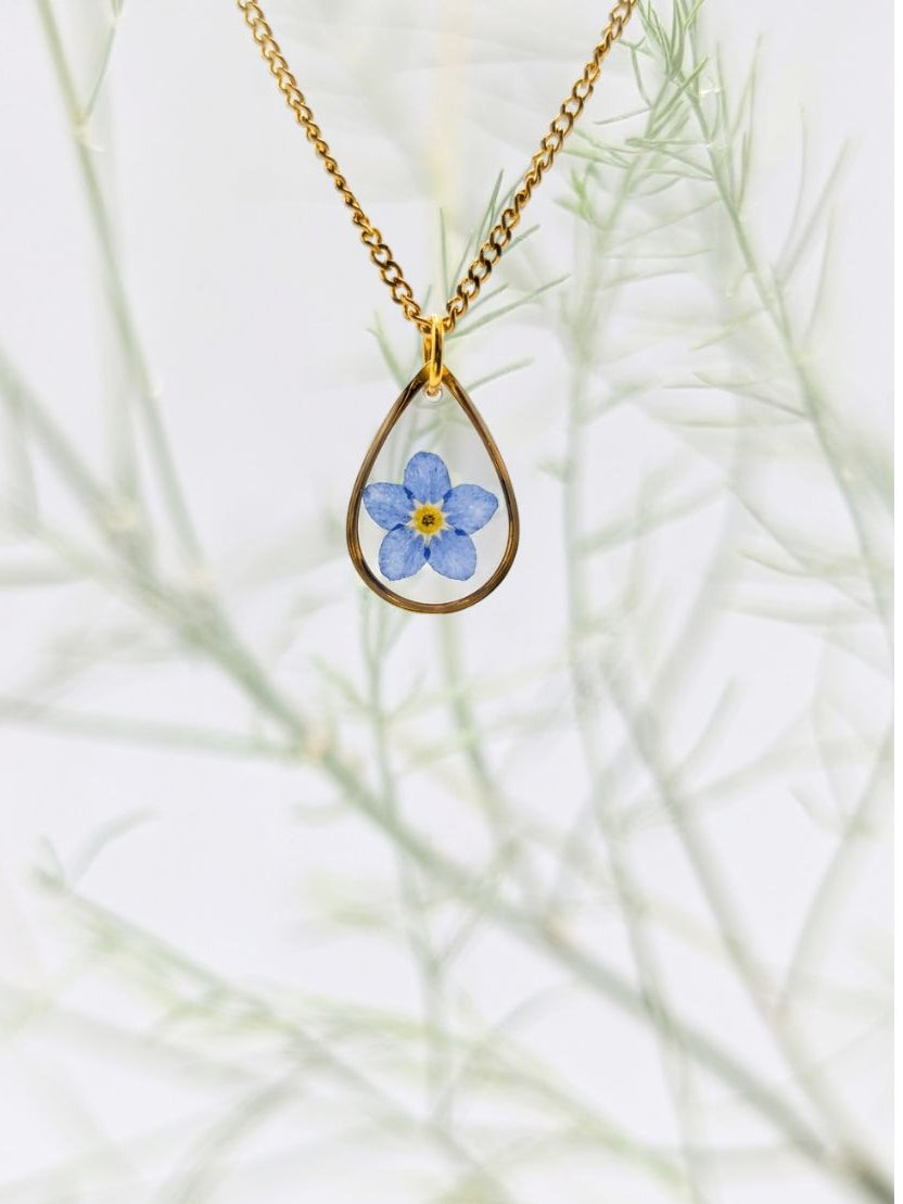 Gold necklace with a teardrop pendant featuring a blue flower on a white background