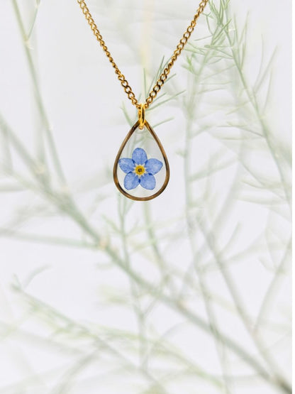 Gold necklace with a teardrop pendant featuring a blue flower on a white background