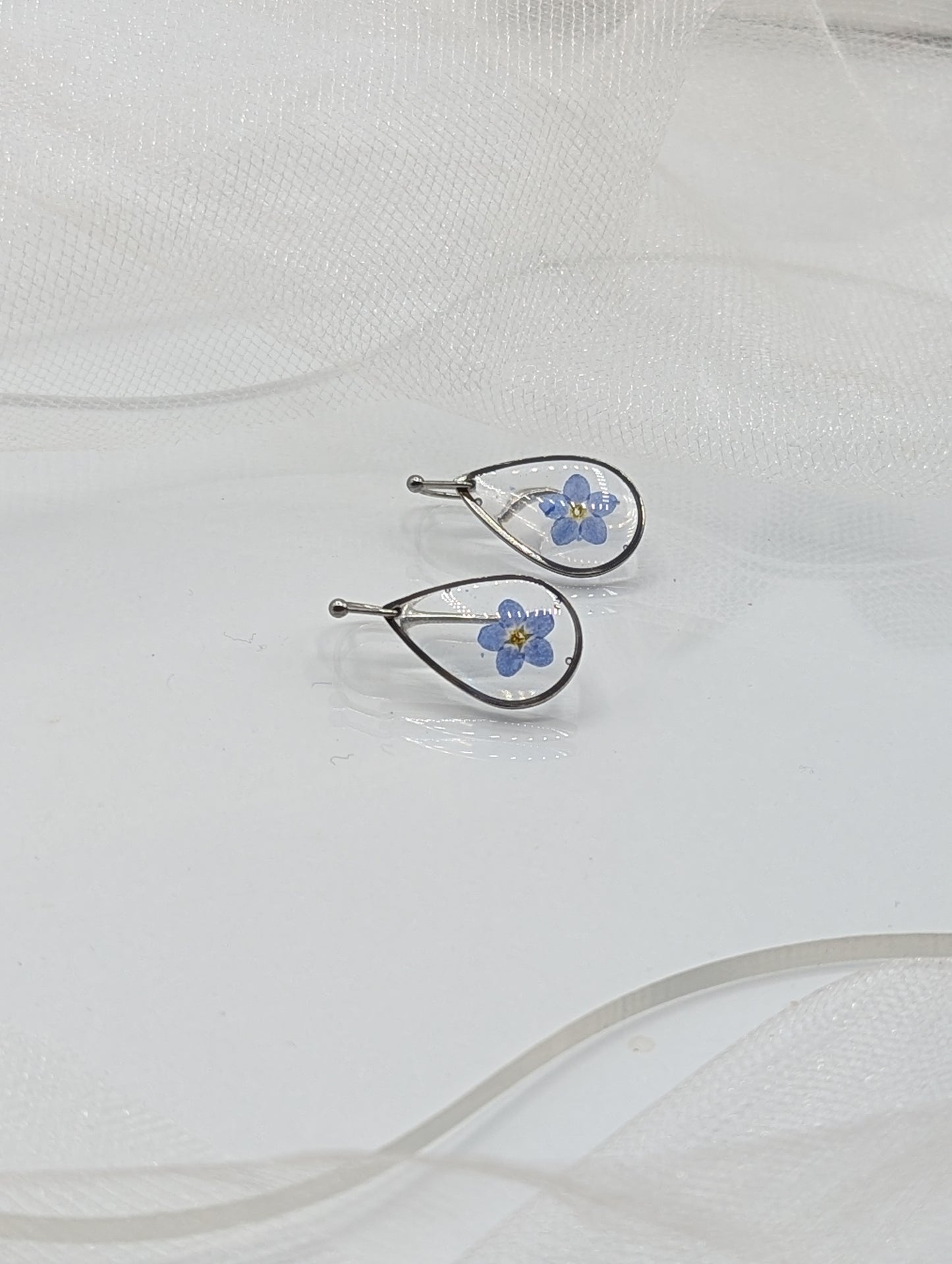 Pair of silver earrings with blue floral designs on a white fabric background