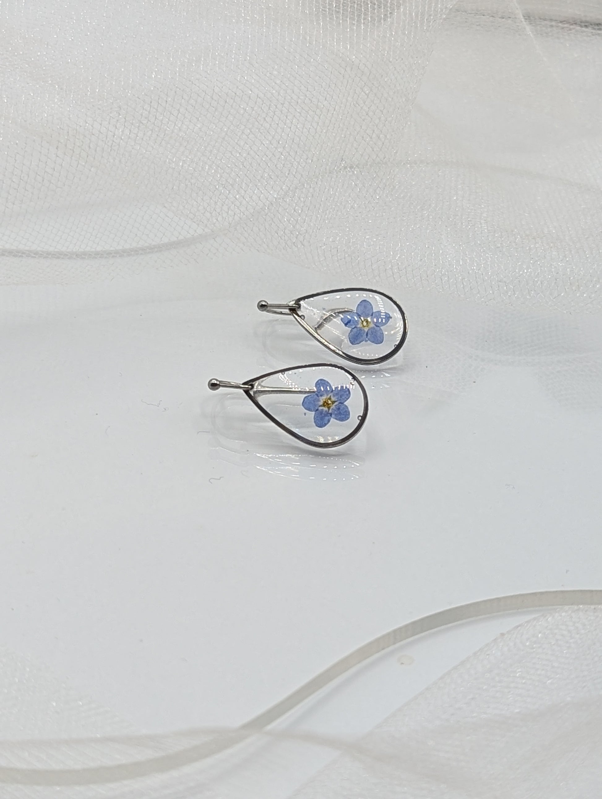 Pair of silver earrings with blue floral designs on a white fabric background