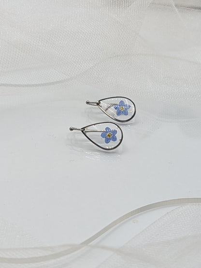 Pair of silver earrings with blue floral designs on a white fabric background