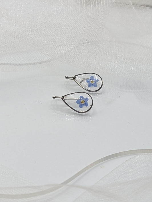Pair of silver earrings with blue floral designs on a white fabric background