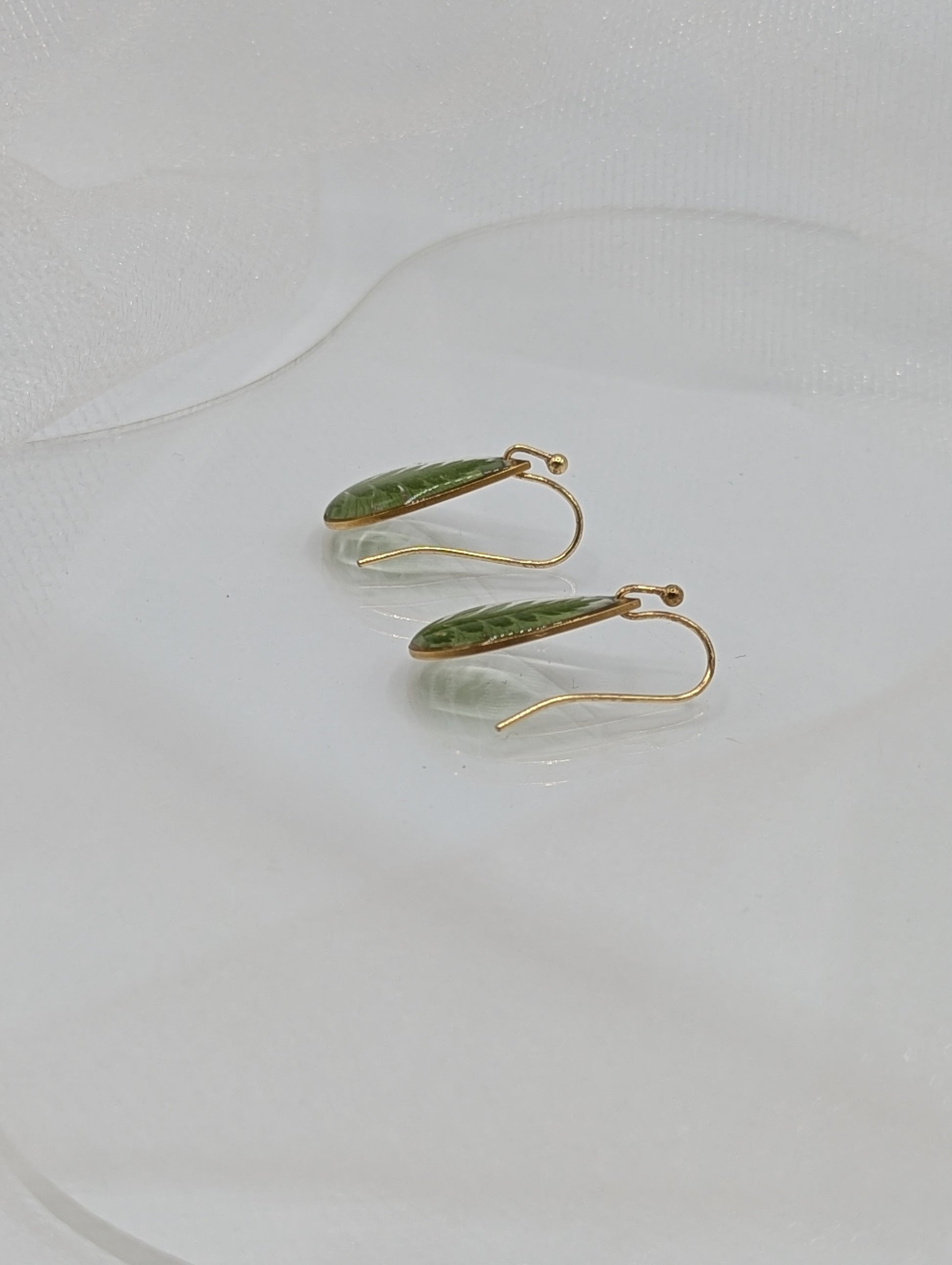 Gold earrings with green leaves on a white background