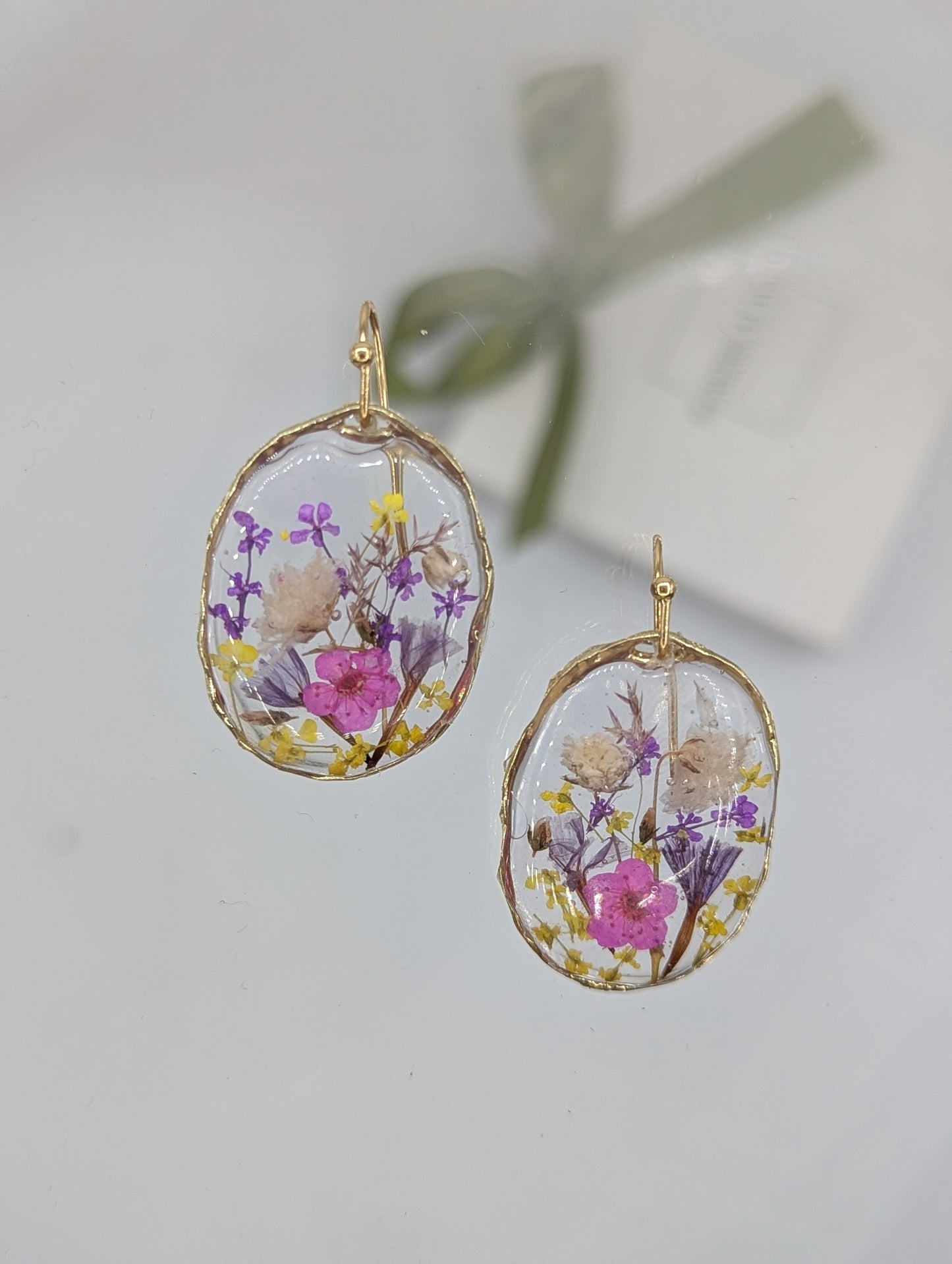 Oval-shaped earrings with floral design on a light gray background