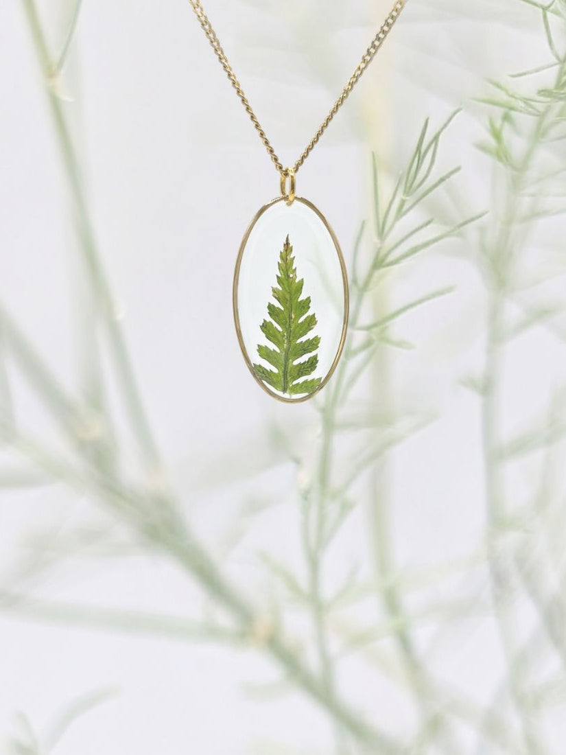 Necklace with a pendant featuring a pressed fern on a light background