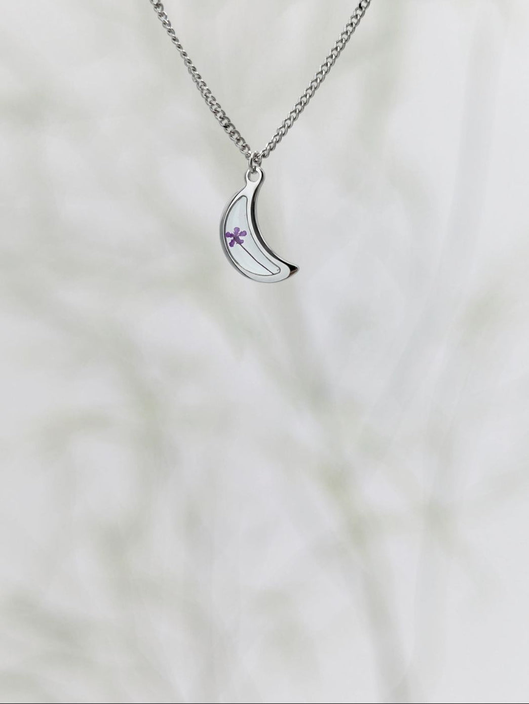 Silver necklace with a crescent moon pendant on a white background