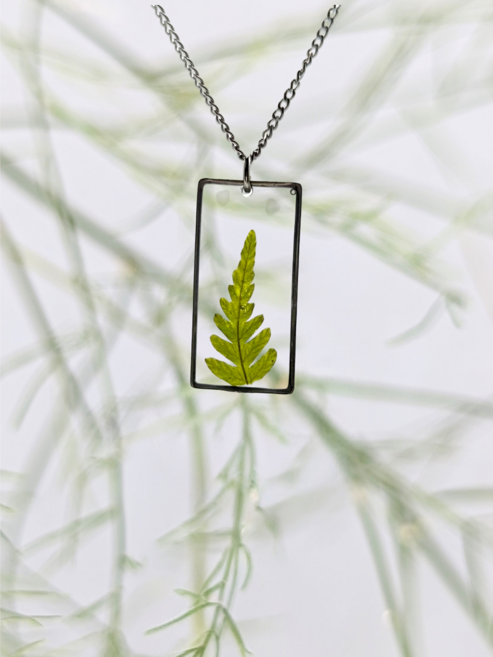 Necklace with a rectangular pendant featuring a pressed green leaf against a blurred natural background