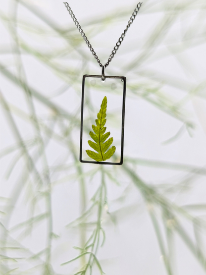 Necklace with a rectangular pendant featuring a pressed green leaf against a blurred natural background