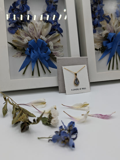 Dried flowers with blue ribbons and a necklace on a white surface.