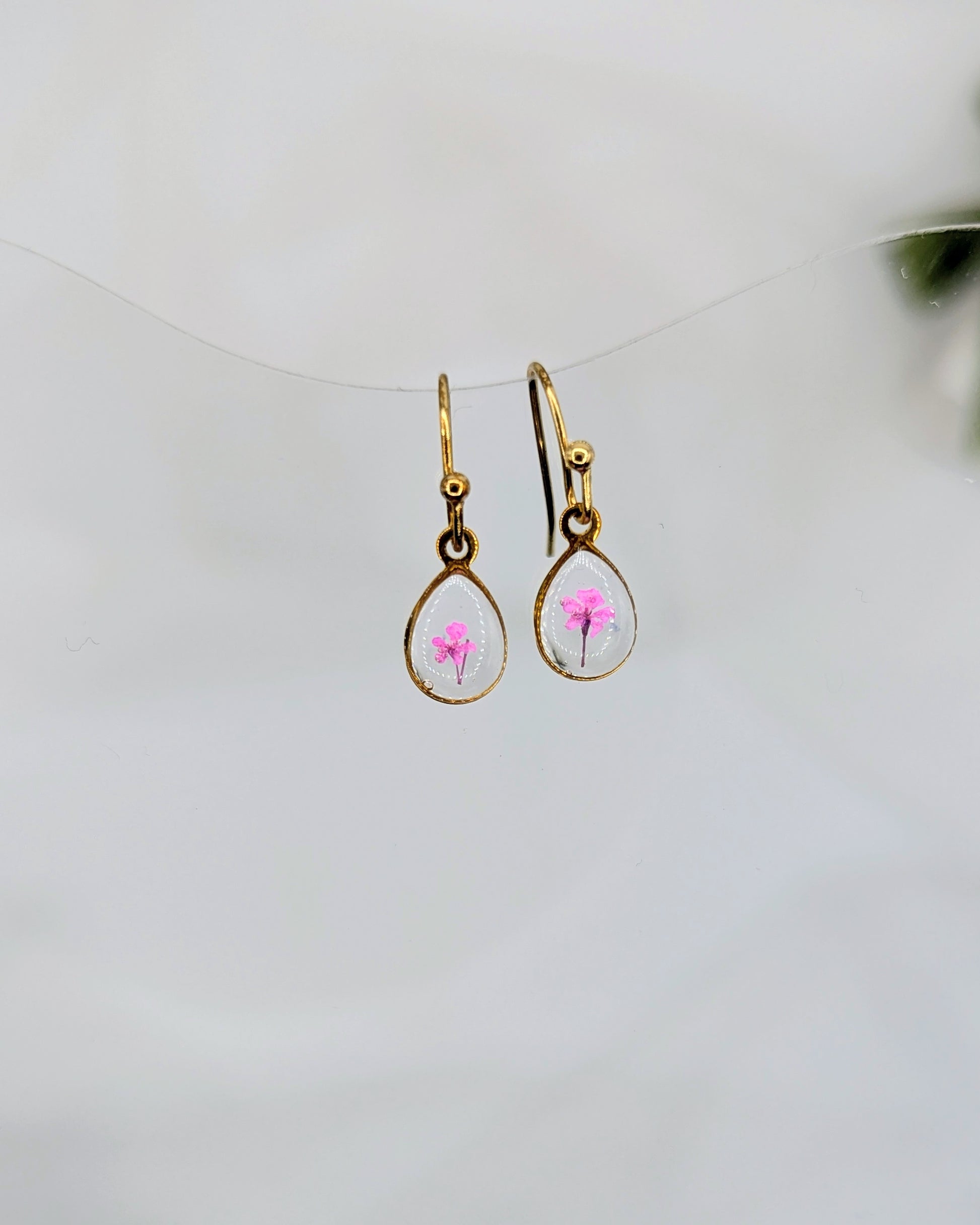 Gold earrings with pink floral design on a white background
