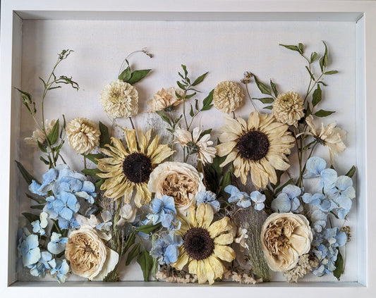 Decorative arrangement of pressed flowers in a white frame on a wooden surface