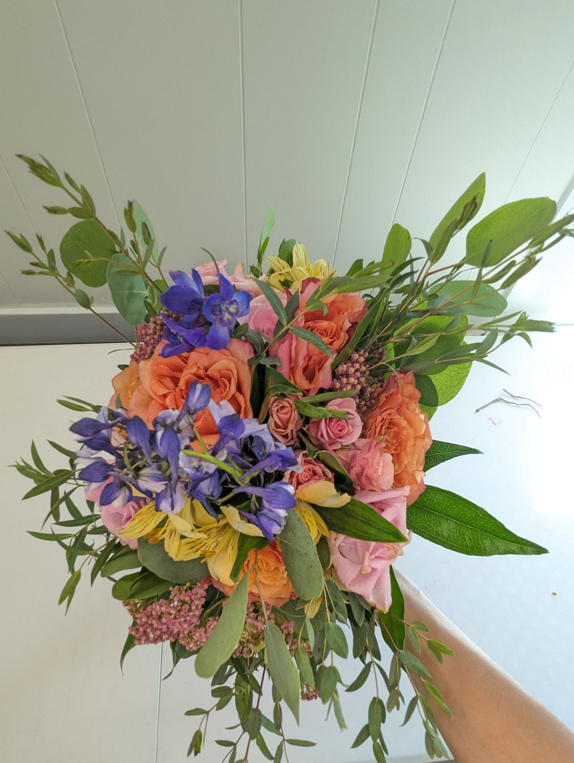 Colorful bouquet of flowers held by a person against a white wall.